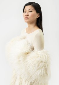 Haut à manches longues écru associé à un vêtement en fourrure crème duveteux et texturé, présentant un design volumineux et une apparence douce.