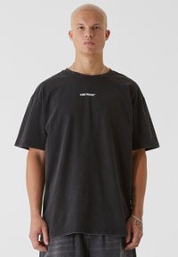 Černé oversized tričko vyrobené z měkké bavlněné látky s kulatým výstřihem a bílým logem "LOST YOUTH" vytištěným na středu hrudi.