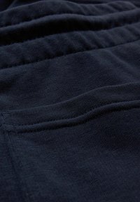 Gros plan sur un tissu bleu foncé montrant des coutures détaillées et une texture, probablement une partie d'un vêtement ou d'un habit.