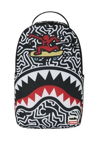 Mochila con un diseño abstracto en blanco y negro, un gráfico rojo y amarillo de una figura surfeando, y un patrón de dientes de tiburón blancos en la parte inferior.