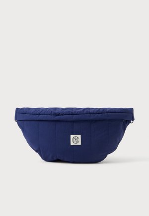 Tumed sinise värvi kootud vöötasku, mille esifailil on valge ruuduline logo, lihtsa ja voolujoonelise disainiga ning rullitav sulgemine.