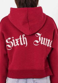 Felpa rossa cropped con cappuccio regolabile, con la scritta bianca "Sixth June" sulla schiena. Tessuto morbido e dettagli in costina sull'orlo.
