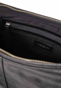 Interno di una borsa in pelle nera che mostra una tasca con cerniera e foderatura in tessuto, con etichetta del marchio cucita, all'interno della chiusura con cerniera superiore aperta.