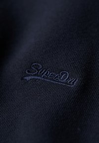 Maglione lavorato a maglia blu navy con un tessuto testurizzato e un logo "SuperDry" in rilievo dello stesso colore sul davanti.