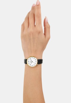Black leather strap watch featuring a round gold-tone case, white dial, and black Arabic numerals. Hands display hours and minutes.