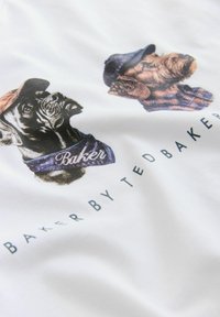 Dvaja psi so šiltovkami a šálmi s textom "Baker", vytlačeným nad textom "Baker by Ted Baker" na bielom látke.