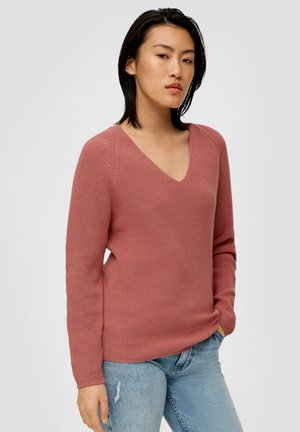 Rosa gestrickter Pullover mit V-Ausschnitt, gerippter Textur und langen Ärmeln. Kombiniert mit hellblauen Jeans.