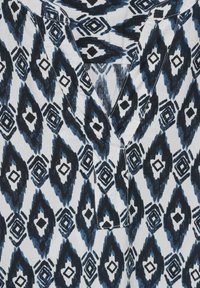 Katoenen shirt met een blauw-wit geometrisch patroon, voorzien van een open V-hals en korte mouwen, met nadruk op diamant- en bladvormen.