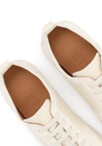 Λευκά sneakers χαμηλού τύπου με ταμπά εσωτερικές σόλες, κορδόνια στο μπροστινό μέρος και θηλάκια στο πίσω μέρος, τοποθετημένα δίπλα δίπλα σε λευκό φόντο.