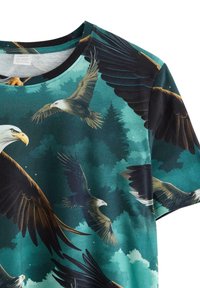 Kortärmad T-shirt i teal tyg med ett tryck av örnar och träd, med detaljerade mönster och rund halsringning.