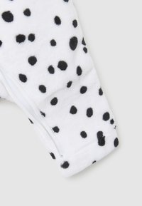 Weißer Fleece-Stoff mit schwarzen Pünktchen; verfügt über einen Reißverschluss und eine strukturierte Oberfläche für Wärme.