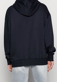 Sweatshirt noir à capuche avec une coupe décontractée, ourlet côtelé et manches longues, fabriqué en tissu doux. Coutures visibles avec une texture lisse.
