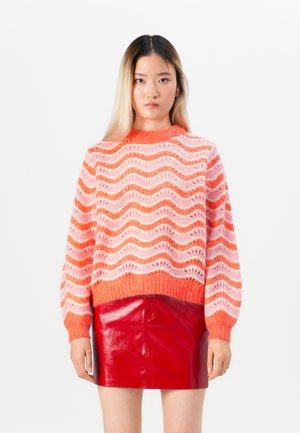 Strikket sweater med et bølget mønster i orange, pink og hvid. Har en rund halsudskæring og lange, puffede ærmer. Matchet med en skinnende rød lædernederdel.