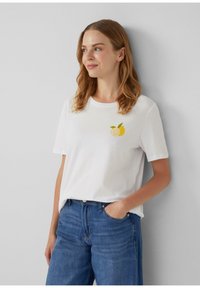 T-shirt en coton blanc avec un graphique de citron et de lime sur la poitrine, manches courtes et encolure ronde, associé à un jean en denim bleu.