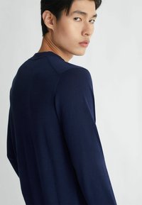Maglietta a maniche lunghe blu navy con scollatura a girocollo, texture morbida e silhouette aderente. Caratterizzata da maniche raglan e dettagli di cucitura sottili.
