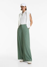 Un cap blanc, une chemise polo à manches courtes blanche et un gilet sans manches en tricot. Un pantalon large à carreaux verts, ample. Des chaussures blanches.