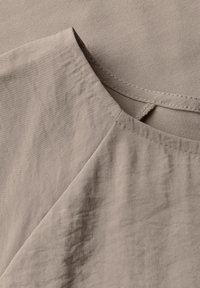 Lys beige beklædning med en blød tekstur, subtile rynker og en bådformet halsudskæring med åben rygdesign.