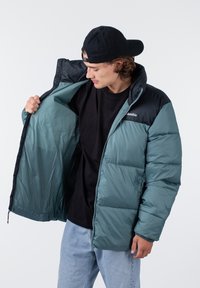 Doudoune teal avec un dos noir, fermeture éclair sur le devant et poches intérieures. Présente un design matelassé et une texture lisse et brillante.