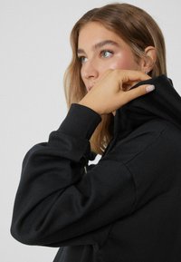 Felpa nera con cappuccio, caratterizzata da un collo alto e polsini a coste. Tessuto di cotone morbido con una vestibilità ampia e dettagli di cucitura resistenti sulle cuciture.
