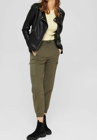 Black leather motorcycle jacket, pale yellow ribbed top, olive green cargo joggers with elastic cuffs, and black ankle boots.