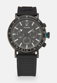 Reloj Timex negro con esfera redonda, correa de goma, escala taquimétrica y tres subesferas, con marcadores y manecillas en blanco.