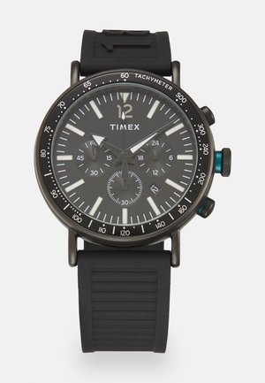 Czarny zegarek Timex z okrągłą tarczą, gumowym paskiem, skalą tachymetryczną i trzema sub-tarczami, z białymi znacznikami godzin i wskazówkami.