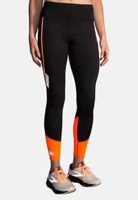 Juodos sportinės legging'os su oranžiniais akcentais, pasižyminčios stilingu dizainu, elastingu juosmeniu ir atspindinčiomis detalėmis šonuose.