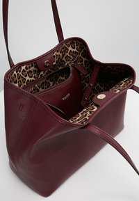 Bordeauxrode leren tas met een gestructureerd oppervlak, voorzien van een voering met luipaardprint en een binnenzak met rits. Inclusief twee lange riemen.