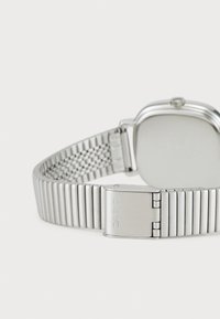 Montre en argent avec un boîtier rectangulaire et un bracelet en maille. Le fermoir est en acier poli, avec un texte de marque gravé sur la boucle.