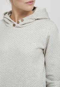 Felpa grigia chiara con un design a motivi che presenta piccoli punti distribuiti uniformemente. Ha un cappuccio con cordino e tre bottoni decorativi.
