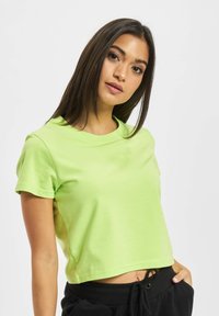 Lime zöld, rövid ujjú, puha anyagból készült cropped póló, kerek nyakkivágással, fekete húzózsinóros rövidnadrággal párosítva.