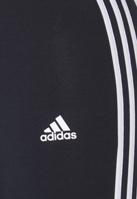 Adidas navy athletic pants with white three-stripe design along the side and a white logo on the lower leg. Smooth texture, fitted shape.