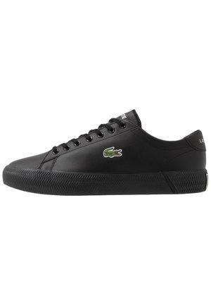 Czarny sneaker niskiego kroju z czarnymi sznurowadłami, teksturowaną podeszwą i małym zielonym logo krokodyla z boku.