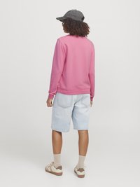 Roze sweatshirt, relaxte pasvorm, katoenmix, geribbelde manchetten, gecombineerd met lichte denim shorts en crèmekleurige sneakers met bruine accenten. Grijze pet achterstevoren gedragen.