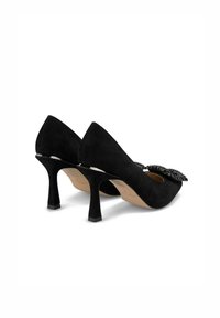 Scarpe con tacco alto in suede nero, con punta a punta e un dettaglio con fiocco decorato con applicazioni nere. Presentano un tacco largo e texturizzato.