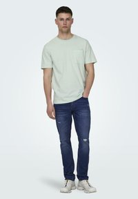 Lys grøn stribet t-shirt med en brystlomme, parret med blå slidte jeans og hvide sneakers. Enkel, afslappet pasform.