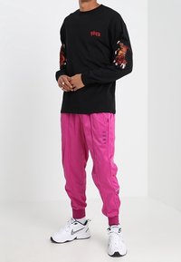 Mustassa pitkähihaisessa paidassa on punaiset tekstit ja tiikerigrafiikkaa hihoissa, jotka on yhdistetty kiiltävään pinkkiin juoksuhousuihin, joissa on sana "GRMY." Valkoiset lenkkarit.