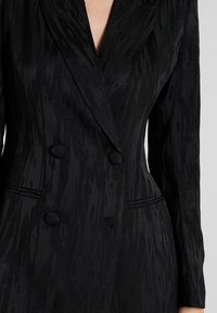 Blazer negro de doble botonadura con un tejido texturizado de patrón similar a la madera, solapas de muesca y dos botones en el frente.