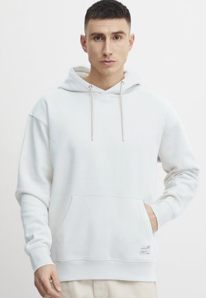 Bijela hoodie s opuštenim dizajnom, vezicama, prednjim džepom i rebrastim manžetama. Izrađena od mekog materijala s suptilnom teksturom.