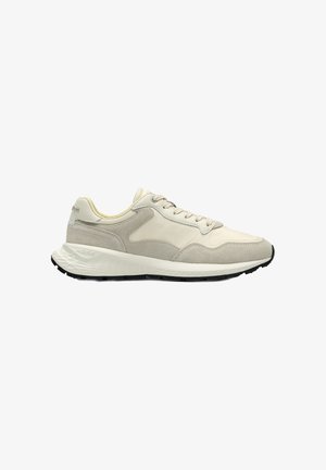Zapatilla deportiva de ante beige y gris claro con parte superior de malla, suela blanca acolchada y suela exterior negra, diseñada para uso casual o deportivo.