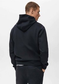 Donker marineblauwe hoodie met een losse pasvorm, voorzien van een grote capuchon, ribbelmanchetten en een zachte textuur. Zichtbare stiksels langs de naden.
