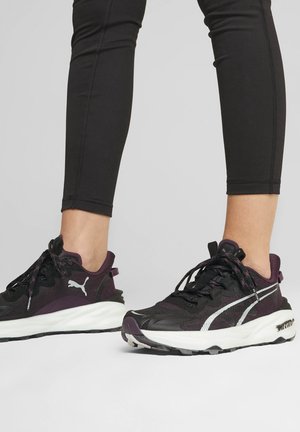 Melna un tumši violeta sporta apavi ar teksturētu materiālu, baltu starpposma daļu, melniem akcentiem un apaļajām šņorēm. Puma logo sānos.