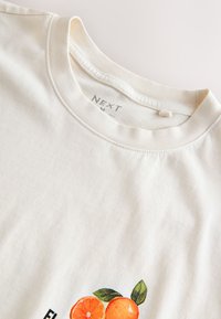 T-shirt in cotone color crema con stampa di mezzi aranci e foglie vicino all'orlo, con scollo tondo e maniche corte.