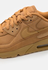 Bruna mockasnörskor med texturerade paneler, med upphöjda detaljer och en framträdande Nike-swoosh. Luftdämpning synlig i sulan.