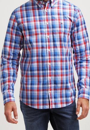 Uomo che indossa una camicia a maniche lunghe con motivo a quadri blu, rosso e bianco e jeans blu scuro.