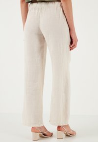 Lichtbeige linnen broek met een ontspannen pasvorm en wijde benen, met een elastische tailleband en rechte zoom. Draagt met beige hakken met bandjes.