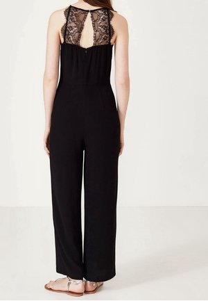 Zwart jumpsuit met kantdetails op de rug, brede pijpen en een ritssluiting. De stof lijkt zacht en soepel, waardoor het ontwerp wordt benadrukt.