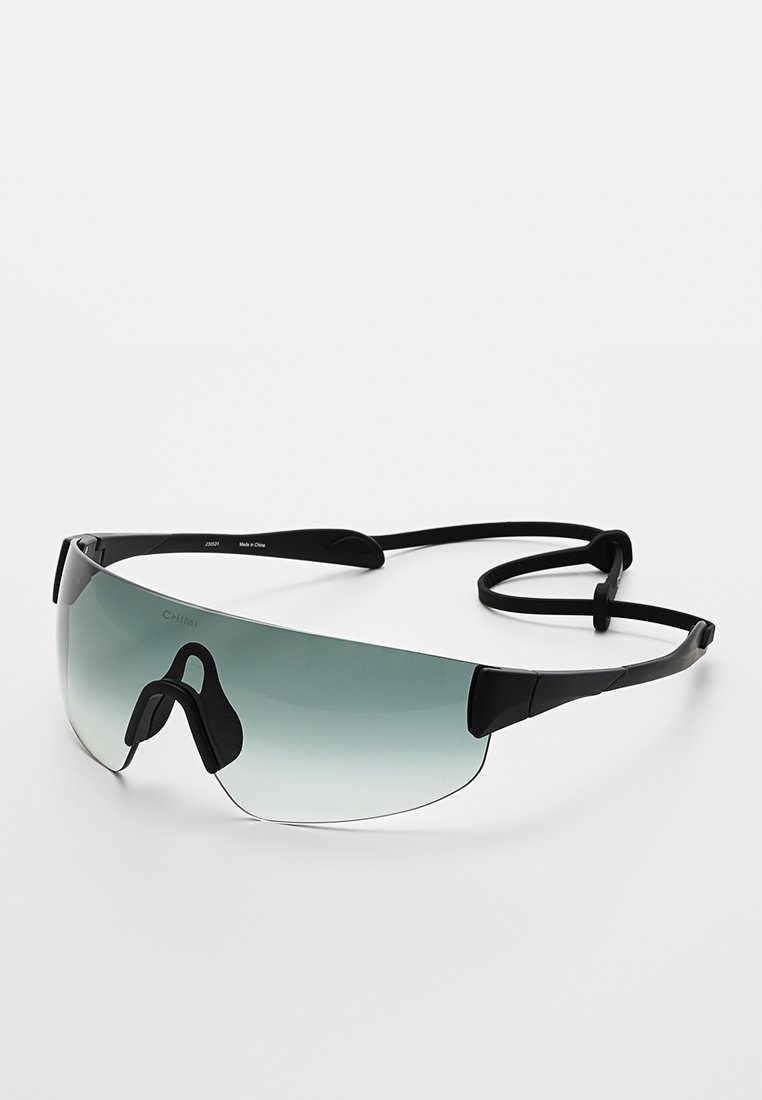Lunettes de sport noires avec verres dégradés, design enveloppant, coussinets en silicone pour le nez et cordon d'attache pour un maintien sécurisé.