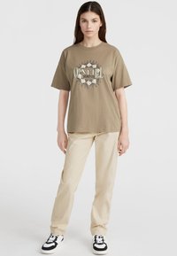 Overgrote bruine T-shirt met een ronde grafische print waarop de tekst "O'Neill Surf Co" in het wit staat, gecombineerd met lichtbeige cargo broeken en zwarte sneakers.