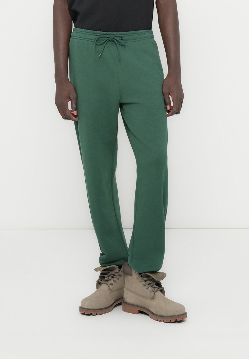 Πράσινο παντελόνι φόρμας με σούρα στη μέση, εφαρμοστή γραμμή και απαλό ύφασμα, συνδυασμένο με καφέ μπότες δέτου τύπου με ανθεκτικό σχέδιο.